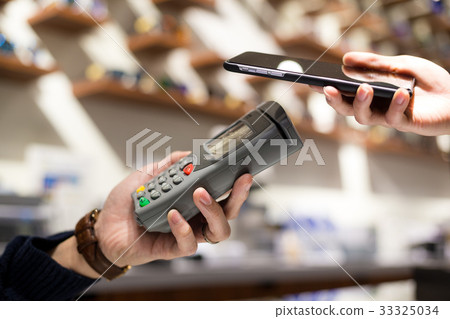 Woman paying with NFC technology on mobile phone in shop Woman paying with NFC technology on mobile phone in shop 33325034