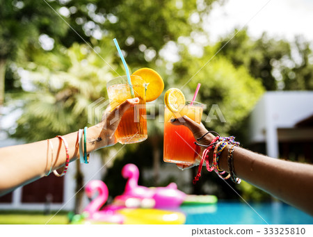 Hands holding juice glasses by the pool summer time 33325810