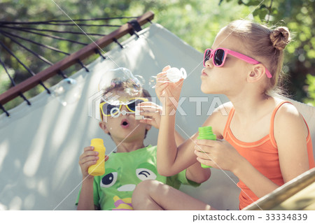 Two happy children lie on a hammock and play with soap bubbles 33334839