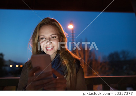 Woman in the city at night holding smartphone Woman in the city at night holding smartphone 33337377