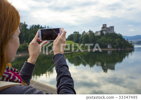 girl taking a picture of a beautiful castle on a lake shore 33347495