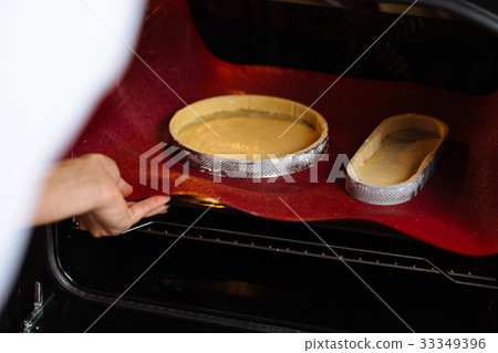 The confectioner puts the biscuit into the oven 33349396