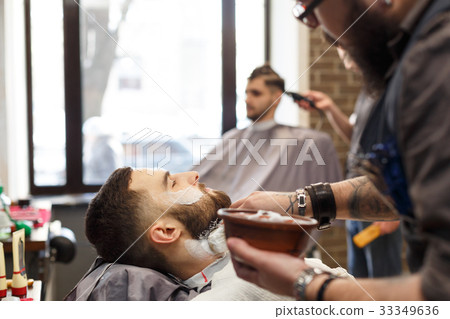 Man getting haircut by hairstylist at barbershop 33349636