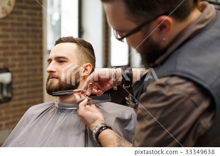 Barber styling beard with scissors to client at 33349638