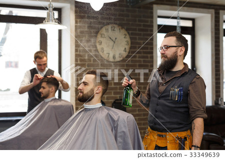 Man getting haircut by hairstylist at barbershop 33349639