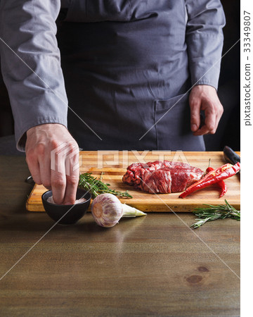 Chef seasoning rib eye steak on wooden board at 33349807