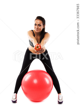 Slim girl wearing training suit with gym ball offering a tomato Slim girl wearing training suit with gym ball offering a tomato 33367665