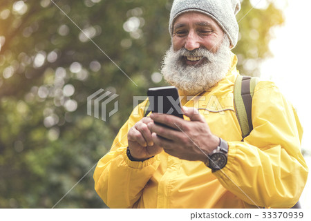 Joyful old man using mobile phone in woodland Joyful old man using mobile phone in woodland 33370939