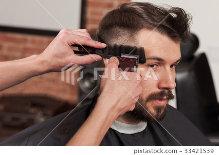 The hands of barber making haircut to young man in The hands of barber making haircut to young man in 33421539