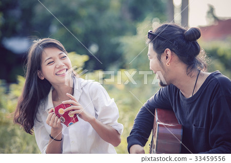younger asian man and woman relaxing playing guitar in park younger asian man and woman relaxing playing guitar in park 33459556