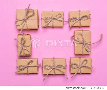 A frame of gift boxes wrapped in kraft paper on a pink background.Flat lay design, top view A frame of gift boxes wrapped in kraft paper on a pink background.Flat lay design, top view 33488332