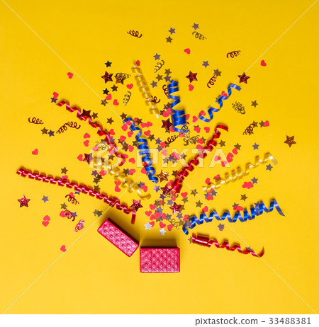 Creative concept with festive decor on yellow. Confetti hearts and stars, ribbons, gift box. 33488381