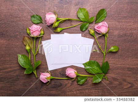 Round frame of delicate flowers. Pink roses on a wooden background. Paper with empty place for text. 33488382