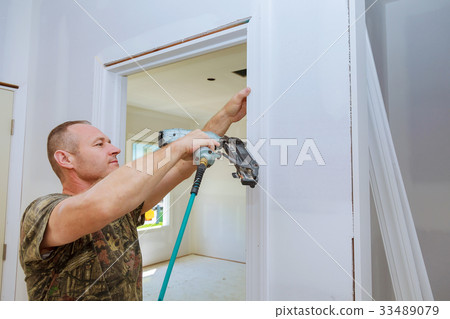 Carpenter brad using nail gun to moldings doors, 33489079