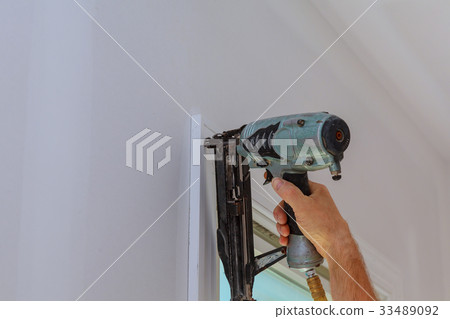 Carpenter using nail gun to moldings on windows Carpenter using nail gun to moldings on windows 33489092