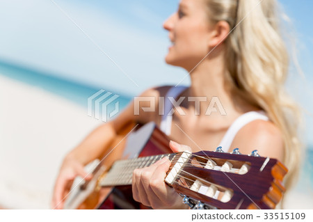 Beautiful young woman playing guitar on beach 33515109