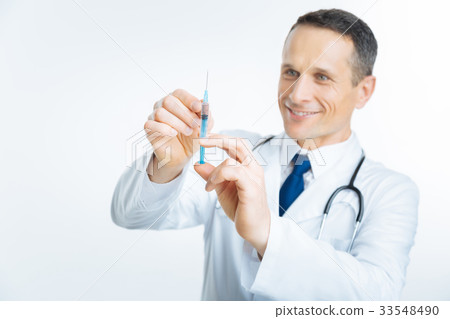 Radiant mature doctor looking at syringe Radiant mature doctor looking at syringe 33548490