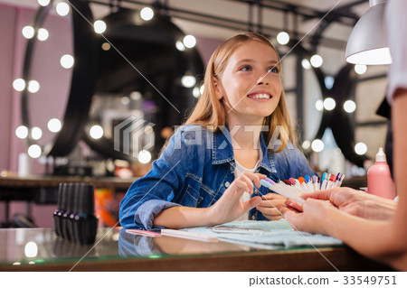 Adorable girl telling manicurist about desired 33549751