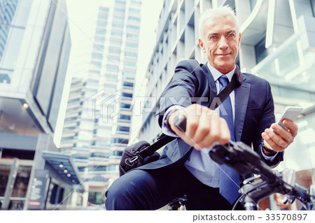 Successful businessman on bicycle with mobile phone Successful businessman on bicycle with mobile phone 33570897
