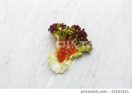 Top view of red caviar on a salad leaf on a light Top view of red caviar on a salad leaf on a light 33581931