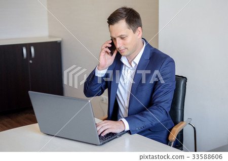Smiling young businessman sitting behind his desk 33588606