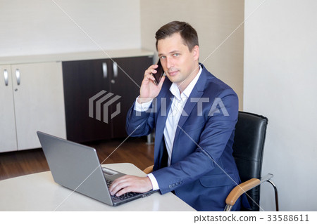 Smiling young businessman sitting behind his desk 33588611