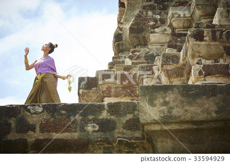 A woman in Thai dress is looking sky and raising her hand at a temple A woman in Thai dress is looking sky and raising her hand at a temple 33594929