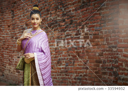 A woman in Thai dress is standing near by a brick wall A woman in Thai dress is standing near by a brick wall 33594932