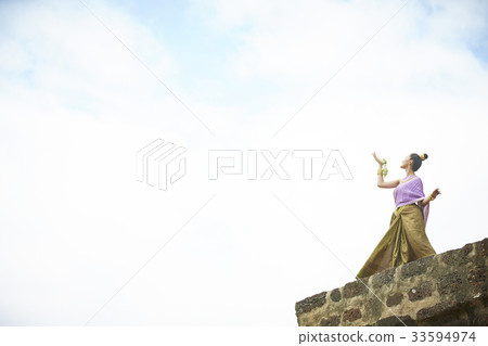 A Thai woman is posing with a Thai dance on a top of a temple 33594974