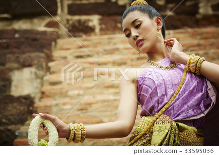 a female dancer in Thai traditional costume is performing outdoors 33595036