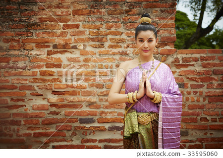 a portrait of smiling thai woman in traditional costume with hands together outdoors 33595060