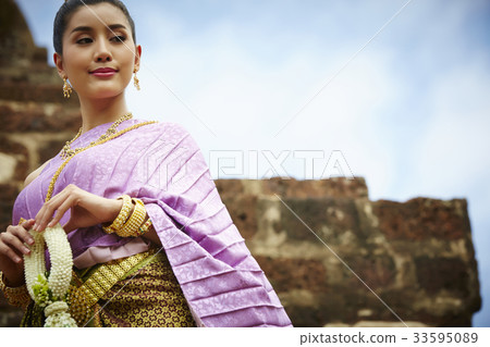 a beautiful woman in thai dress is holding ornament outdoors 33595089