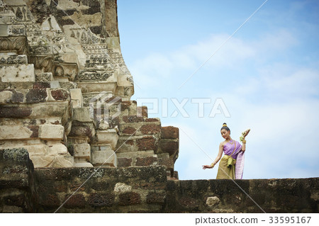A Thai woman is dancing outdoors of a pagoda 33595167