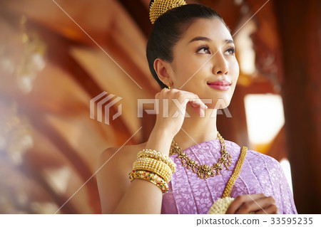 A beautiful Thai woman is touching her face while looking at something. 33595235