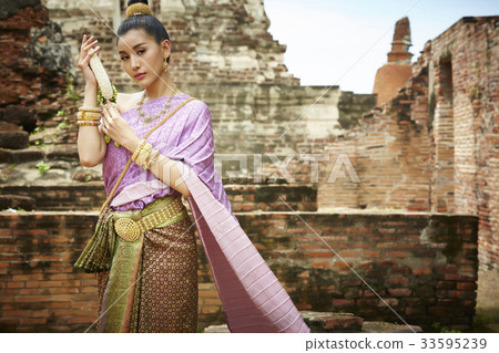 A Thai charming woman is looking at camera while holding an ornament outside. A Thai charming woman is looking at camera while holding an ornament outside. 33595239