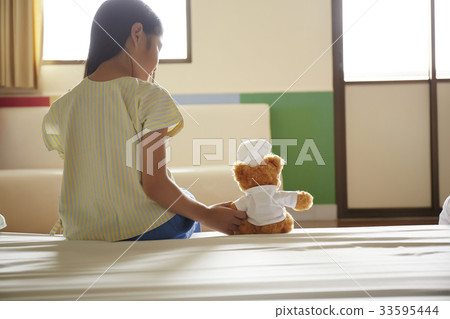 little girl is sitting on bed and looking at teddy bear 33595444