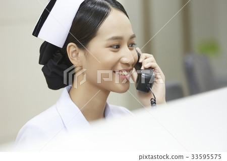 A photo of Asian young nurse talking on phone and smiling in the hospital. 33595575