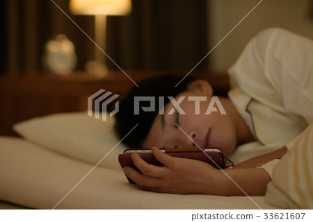 一名婦女在床上的看一個智能手機 33621607