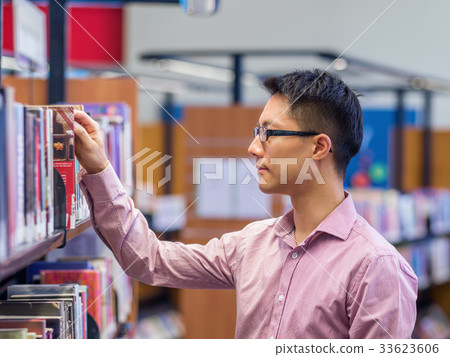 Happy male student picking up books at the library 33623606