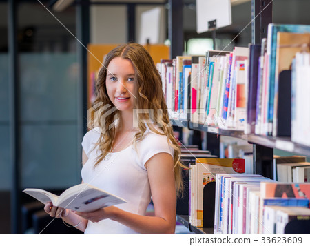 Happy female student holding books at the library Happy female student holding books at the library 33623609