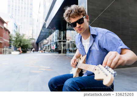 Young musician with guitar in city 33625203