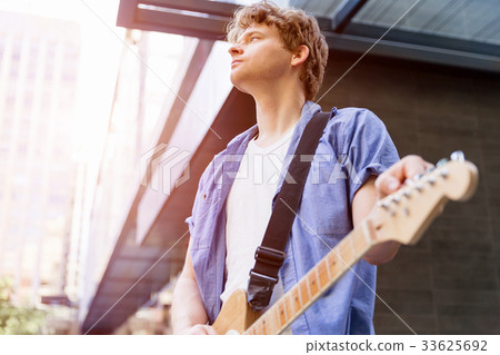 Young musician with guitar in city Young musician with guitar in city 33625692