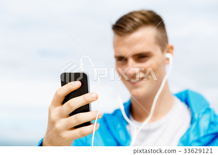 Male runner with his mobile smart phone standing outdoors 33629121