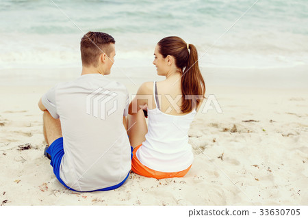 Young couple looking at each other while sitting on beach Young couple looking at each other while sitting on beach 33630705