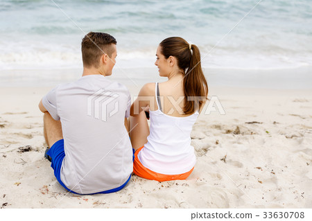 Young couple looking at each other while sitting on beach Young couple looking at each other while sitting on beach 33630708