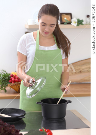 Young caucasian woman in a green apron cooking in 33673148