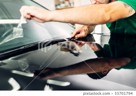 Man installs car paint protection film on hood 33701794