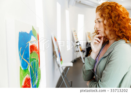 Young caucasian woman standing in art gallery front of paintings Young caucasian woman standing in art gallery front of paintings 33713202