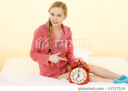 Sleepy woman wearing pajamas holding clock Sleepy woman wearing pajamas holding clock 33727524
