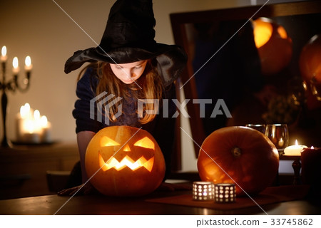 Adorable little girl wearing Halloween costume having fun with carved pumpkin 33745862